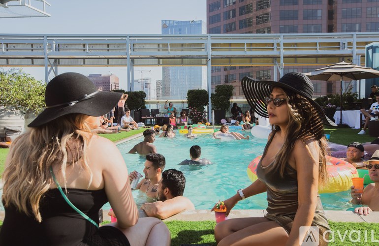 Two women in hats are sitting by a pool with people swimming in the background.