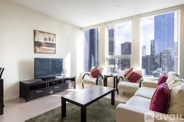 A living room with a television, white couches, and a city view through the windows.
