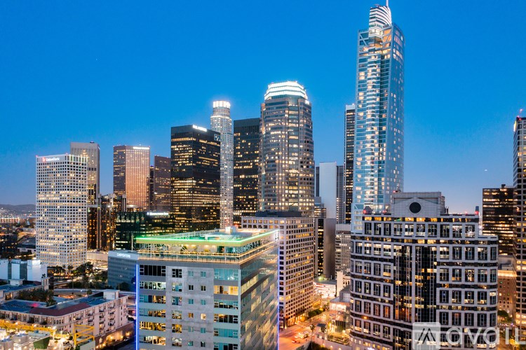 A cityscape at dusk with buildings illuminated against a darkening sky.