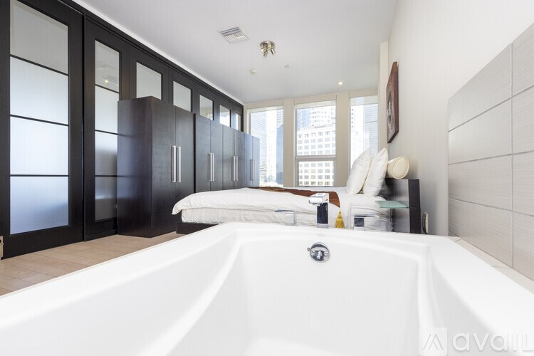 A white bathtub is in a bathroom with a bed and a window.