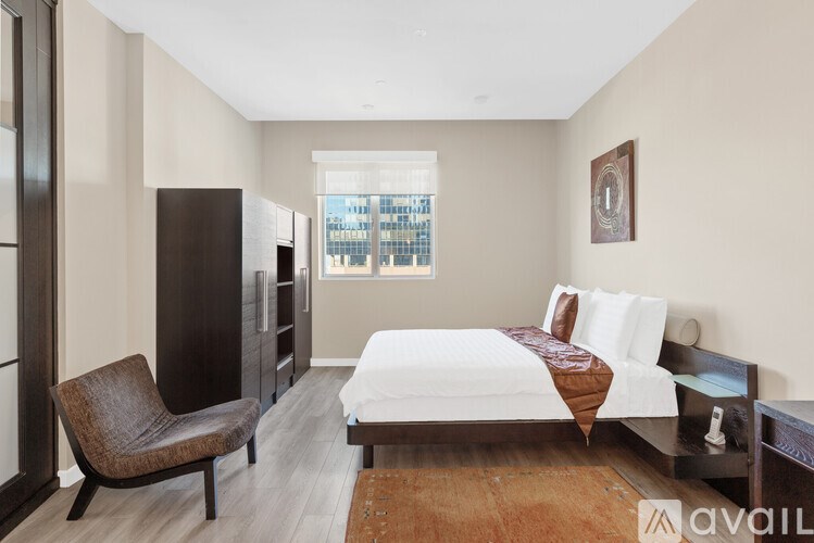 A bedroom with a bed, chair, and a window overlooking a cityscape.