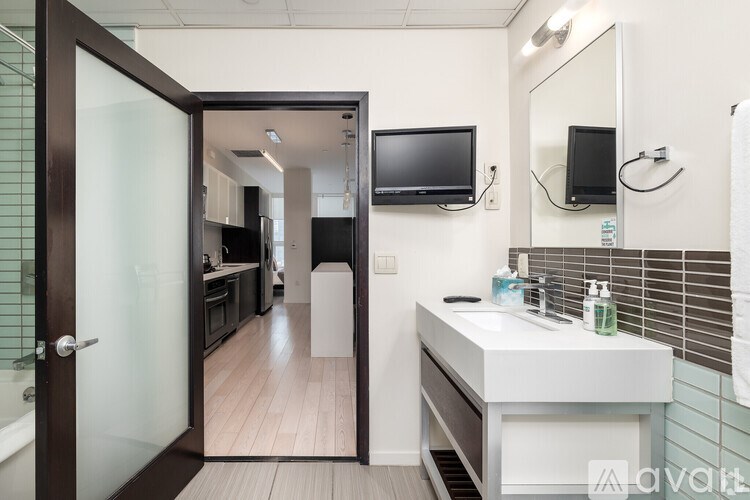 A bathroom with a sink, mirror, and a television mounted on the wall.