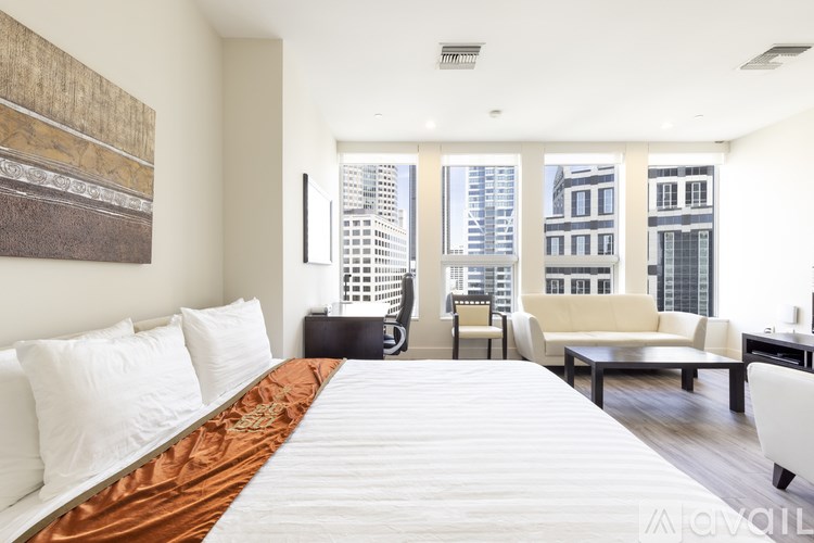 A bedroom with a large bed and a city view through the windows.