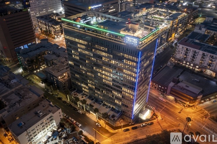 A tall building with a blue light on the side stands out in the city at night.