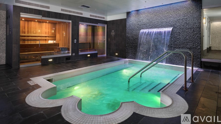 A modern indoor swimming pool with a waterfall feature.