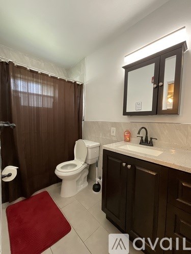 A bathroom with brown shower curtains and a red rug.