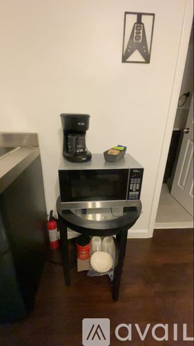A black coffee maker on a black shelf with a picture of a man on the wall.