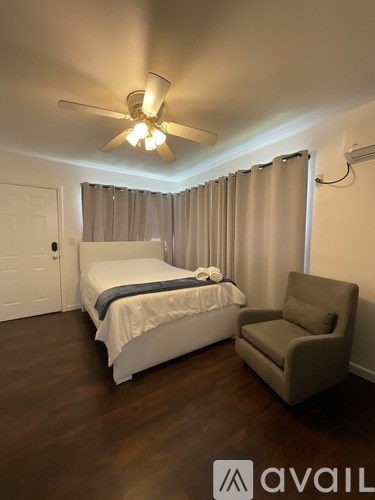 A bedroom with a bed, chair, and ceiling fan.