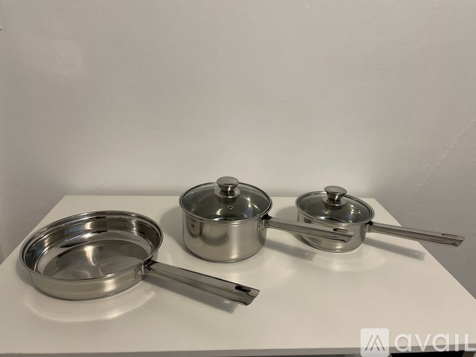 Three stainless steel pots and pans on a white surface.