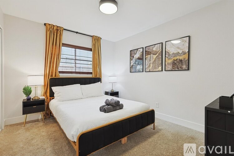 A bedroom with a large bed, a window with curtains, and a nightstand with a lamp.