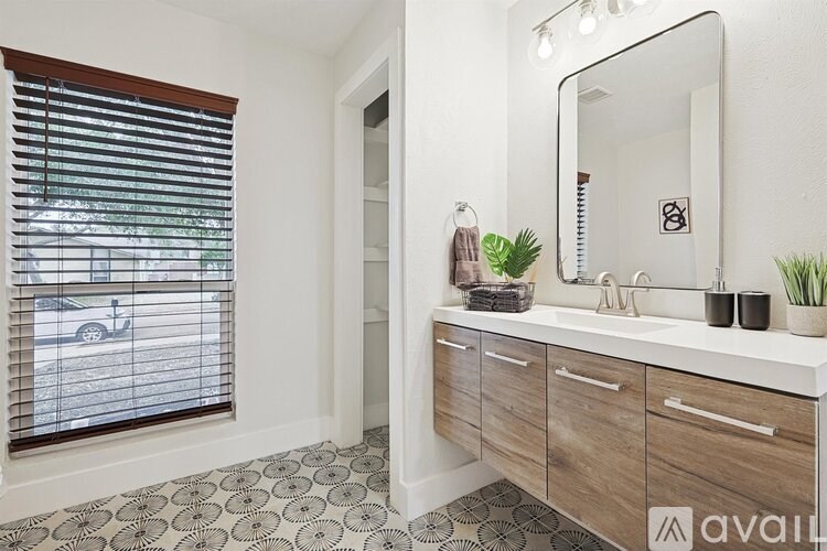 A bathroom with a mirror, sink, and a window with blinds.