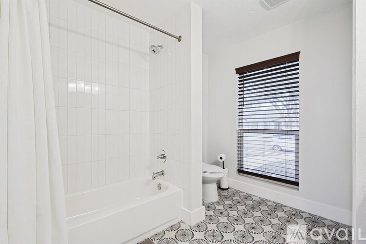 A white bathroom with a patterned floor and a window with blinds.