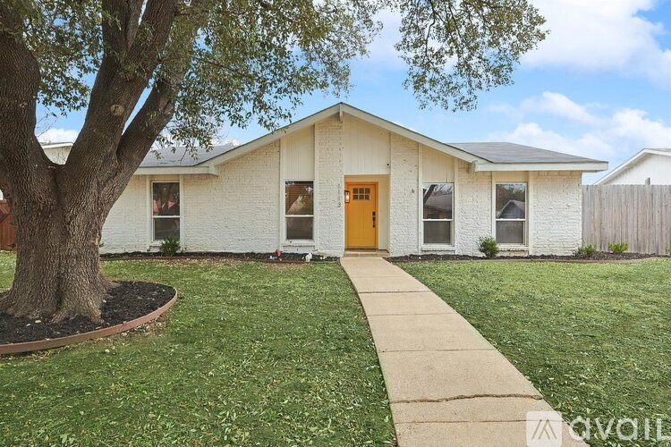 A white house with a brown door and a tree in front.