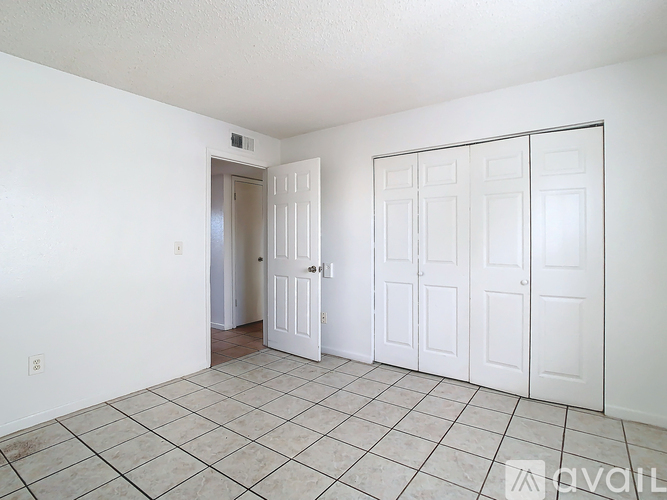 A room with white walls and a tiled floor with a door on the left and three closets on the right.