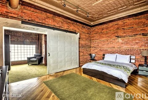 A bedroom with a brick wall and a bed with a white comforter.