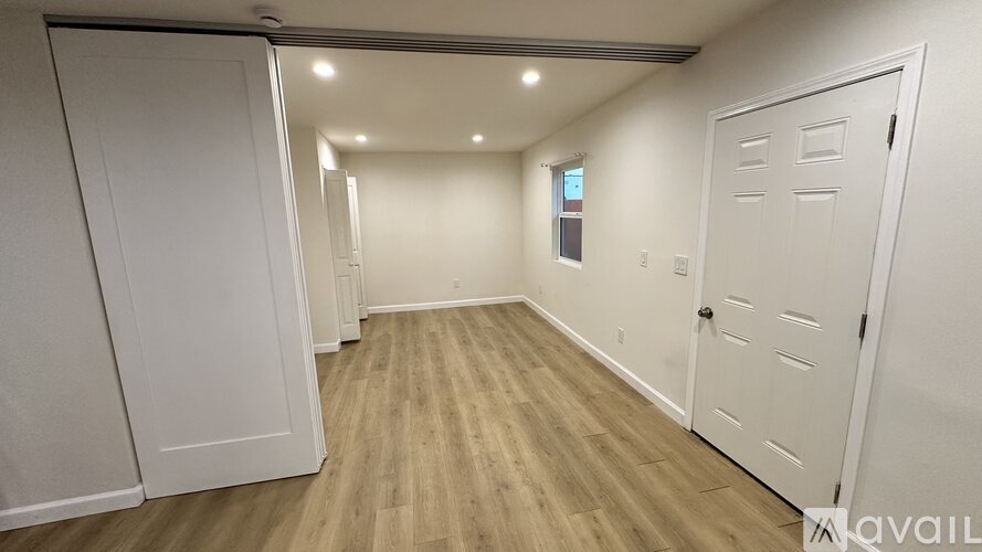A room with white walls and wooden flooring, featuring a white door and a window.