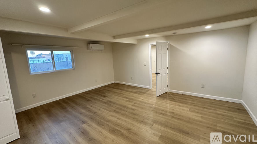 A room with wooden flooring and a window with a view of buildings outside.