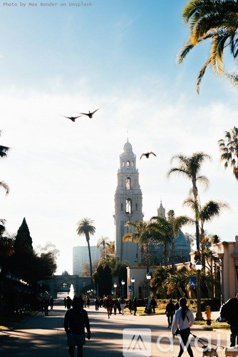 A city street with people walking and a large white tower in the background.