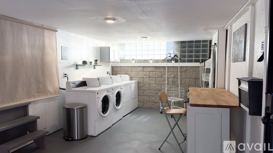 A laundry room with a washer and dryer, a chair, and a trash can.