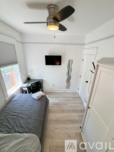 A bedroom with a bed, a ceiling fan, and a television mounted on the wall.