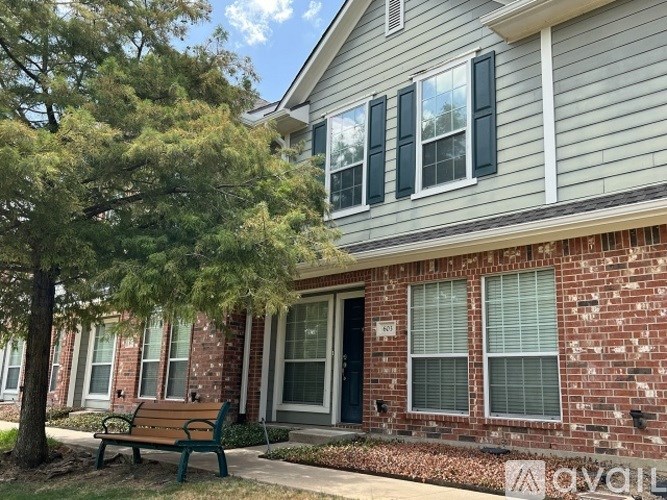 A house with a grey siding and a brick wall with a bench in front.