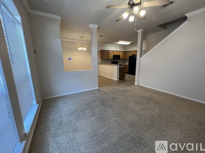 A spacious room with a carpeted floor, a ceiling fan, and a staircase leading to another room.