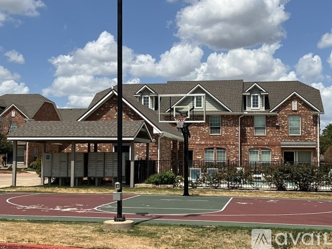 A basketball court is in front of a large brick house.