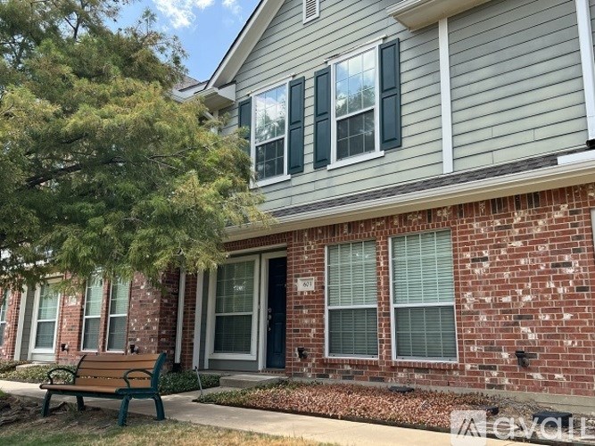 A house with a grey siding and a brick wall with a bench in front.