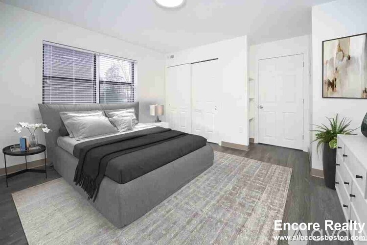 A bedroom with a large bed and a small nightstand with a vase of flowers on it.