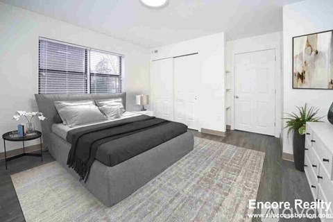 A bedroom with a large bed and a small nightstand with a vase of flowers on it.