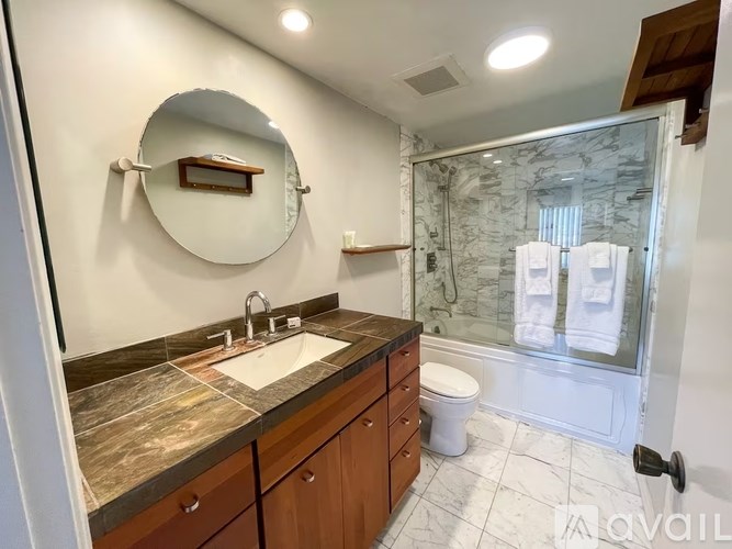 A bathroom with a marble countertop and a round mirror.