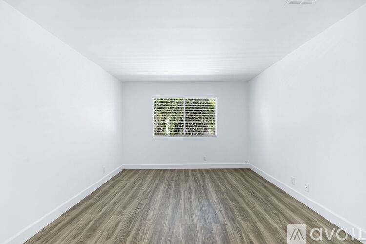 A room with wooden flooring and a window with blinds.