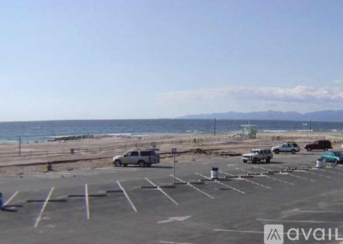A parking lot with several cars and a beach in the background.