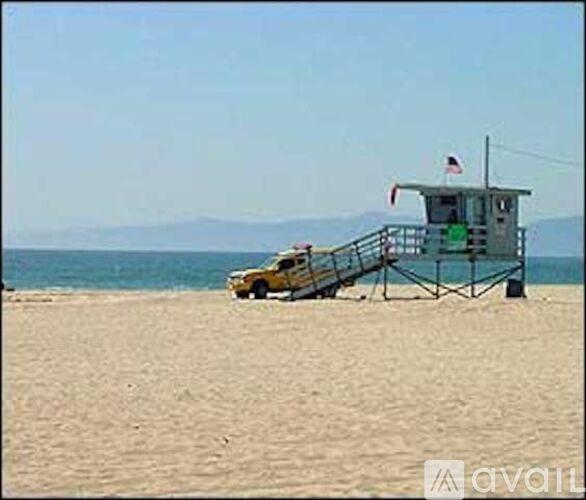 A lifeguard tower sits on a sandy beach with a yellow car parked in front.