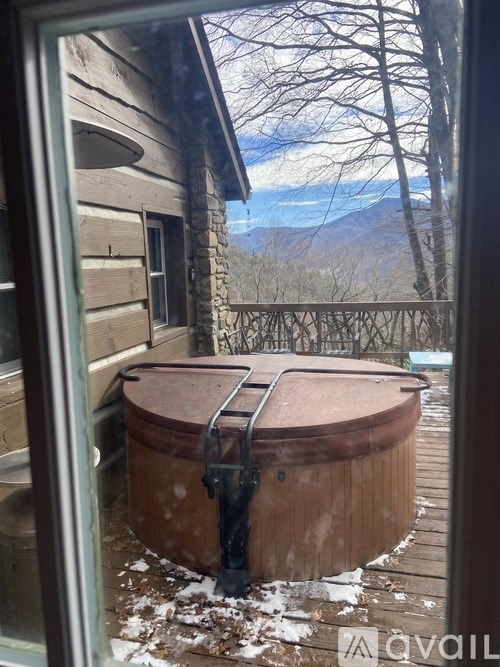 A hot tub sits on a deck with snow on the ground and trees in the background.
