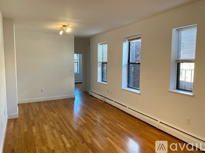 A spacious room with wooden flooring and three windows.