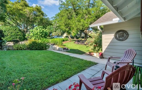 A backyard with a lawn, trees, and a patio with chairs.