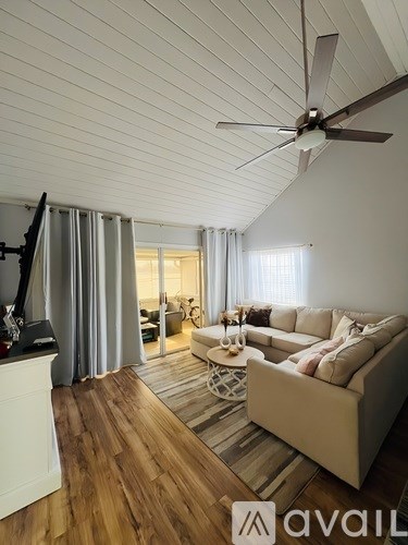 A living room with a beige couch and a ceiling fan.