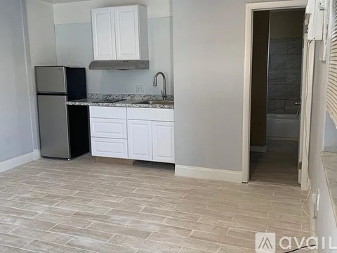 A kitchen with a black fridge, white cabinets, and a marble countertop.