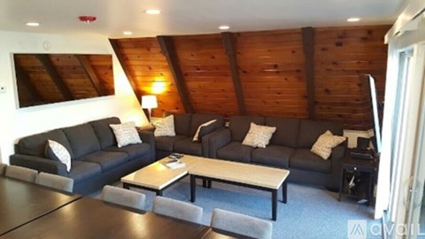 A living room with a black couch and a wooden ceiling.