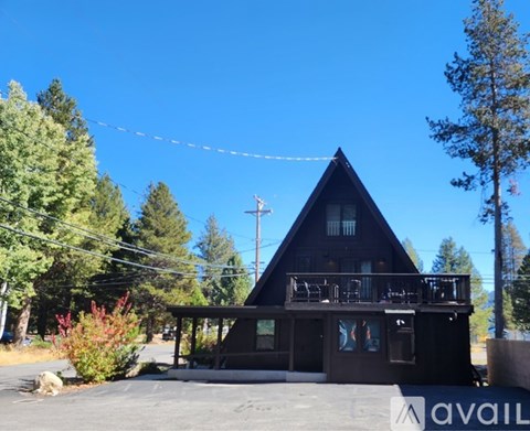 A house with a triangular roof and a balcony is surrounded by trees.