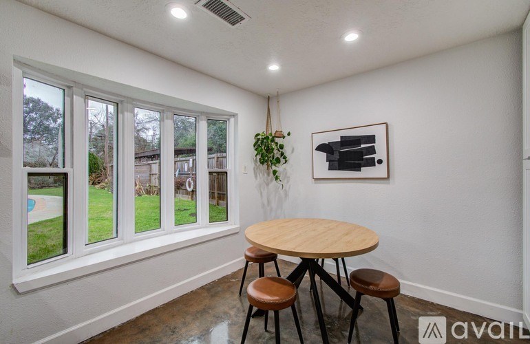 A room with a round table and chairs, a window with a view of a backyard, and a framed picture on the wall.