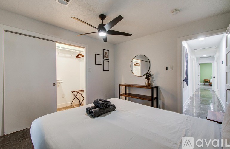 A bedroom with a bed, a mirror, a ceiling fan, and a small table with a plant on it.