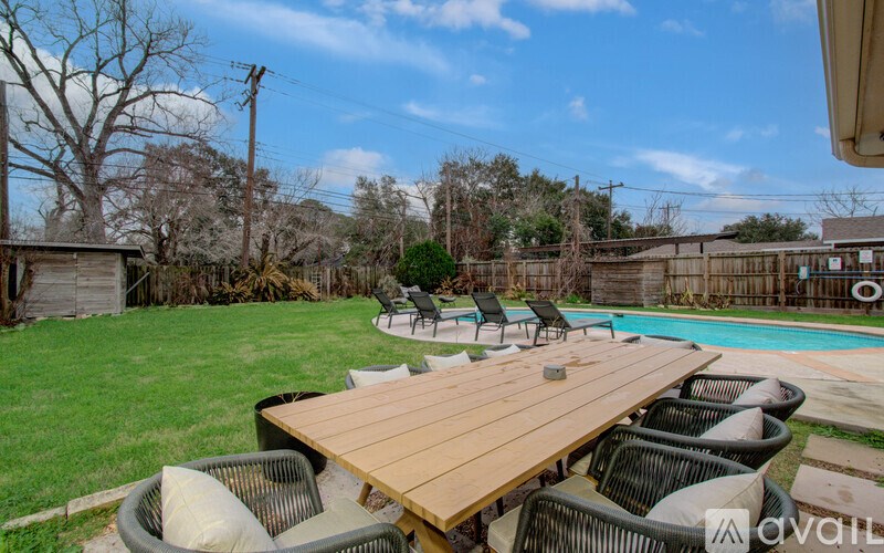 A wooden table is surrounded by chairs in a backyard.