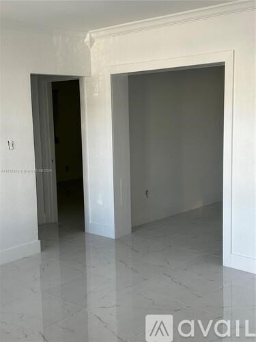 A room with a white floor and walls, and a doorway leading to another room.