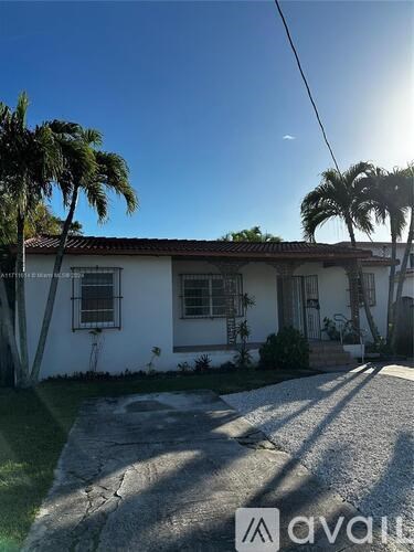 A house with a white exterior and a red roof is surrounded by palm trees.
