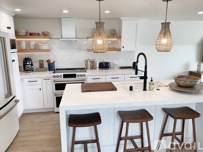 A kitchen with white cabinets and a white countertop with brown stools.