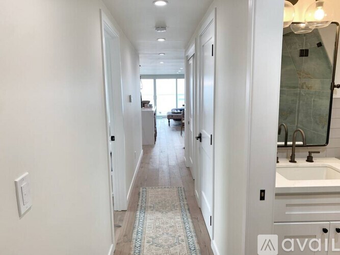 A long hallway with a rug on the floor and a bathroom on the right.