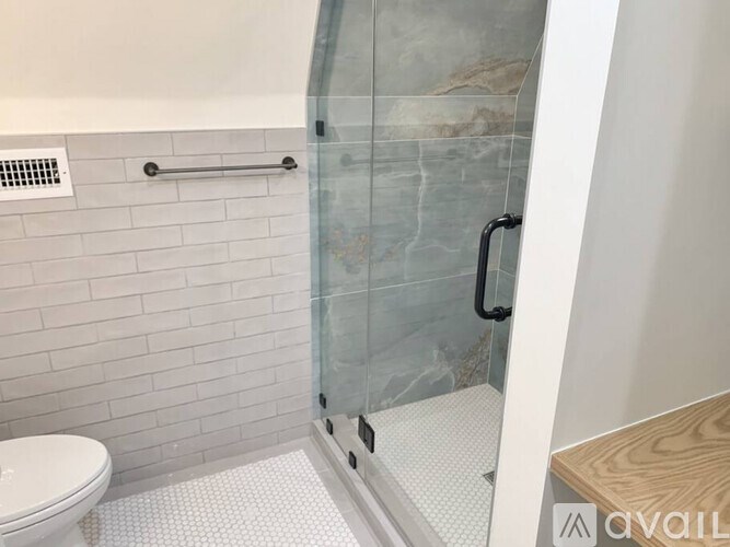 A bathroom with a toilet, a glass shower door, and a white tiled wall.