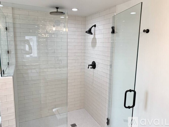 A glass shower stall with a glass door and a black handle.